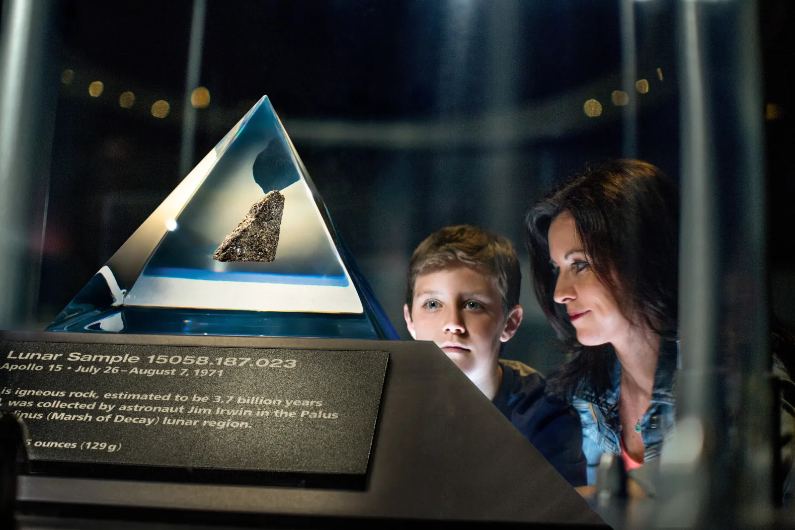 Mother and son looking at an Apollo 15 lunar sample displayed inside a glass pyramid