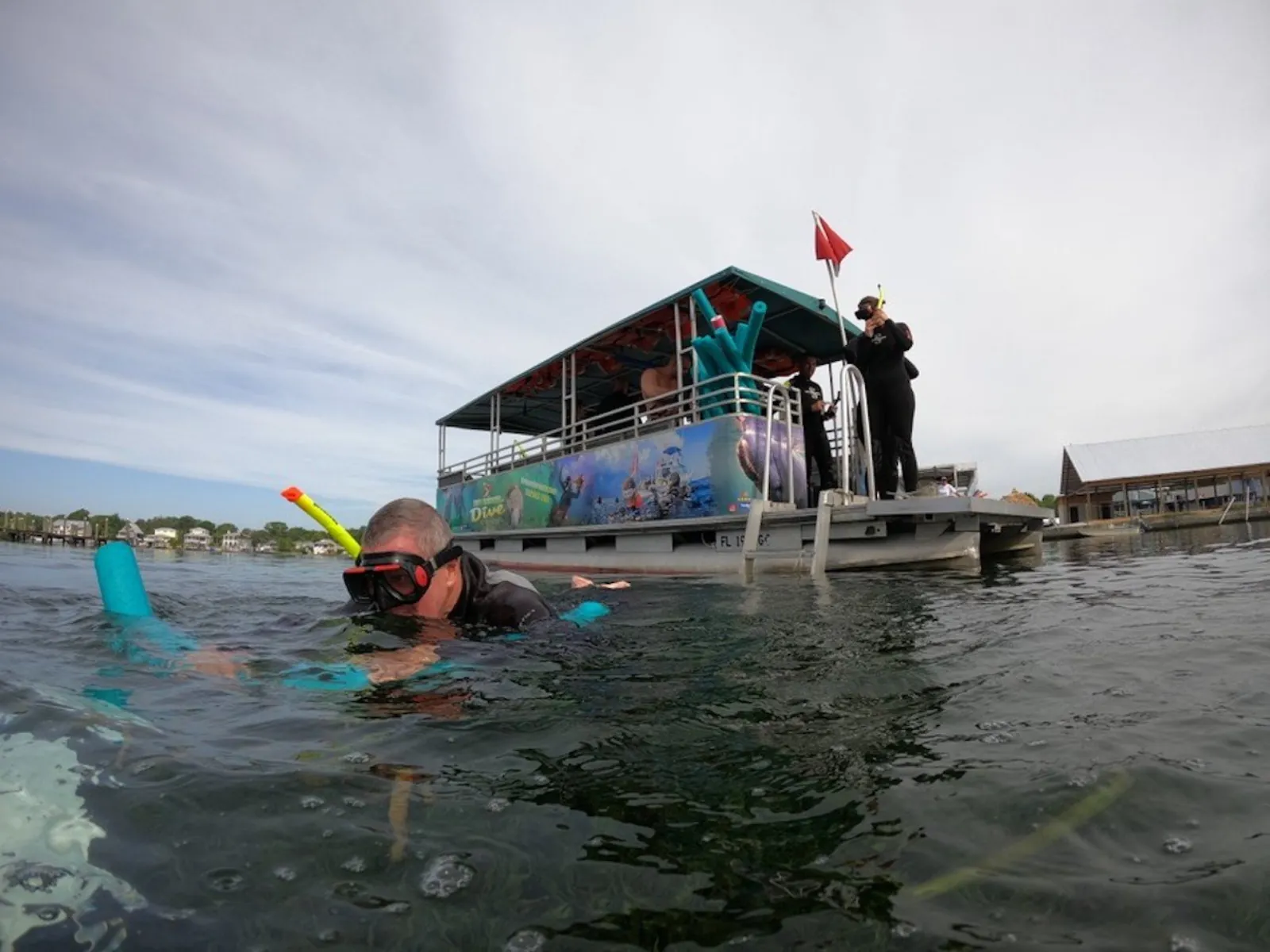 Snorkeler with a foam noodle in the water beside a covered pontoon dive boat
