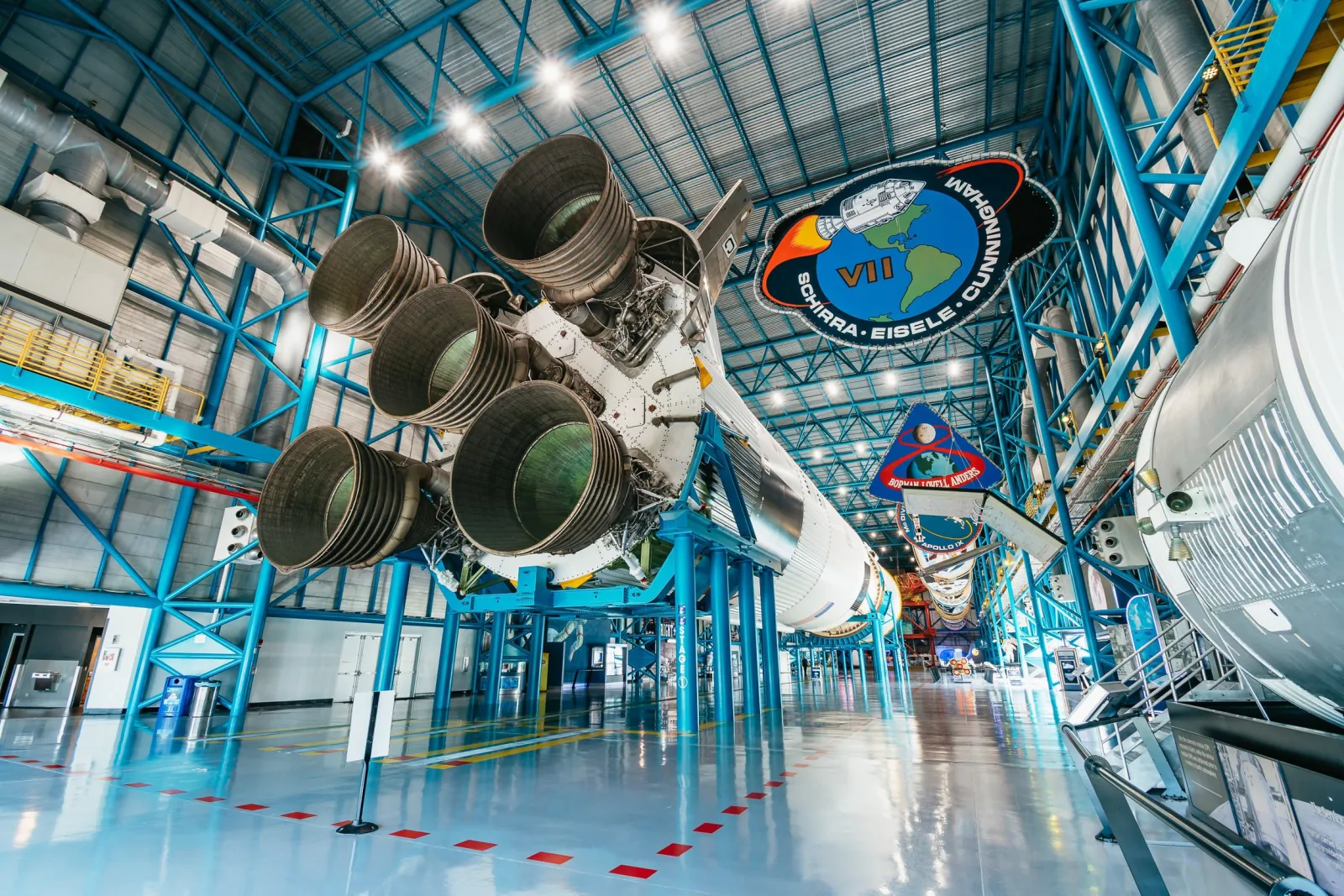 Saturn V rocket engines suspended over the polished floor of the Apollo/Saturn V Center, with Apollo mission patches hanging from the ceiling