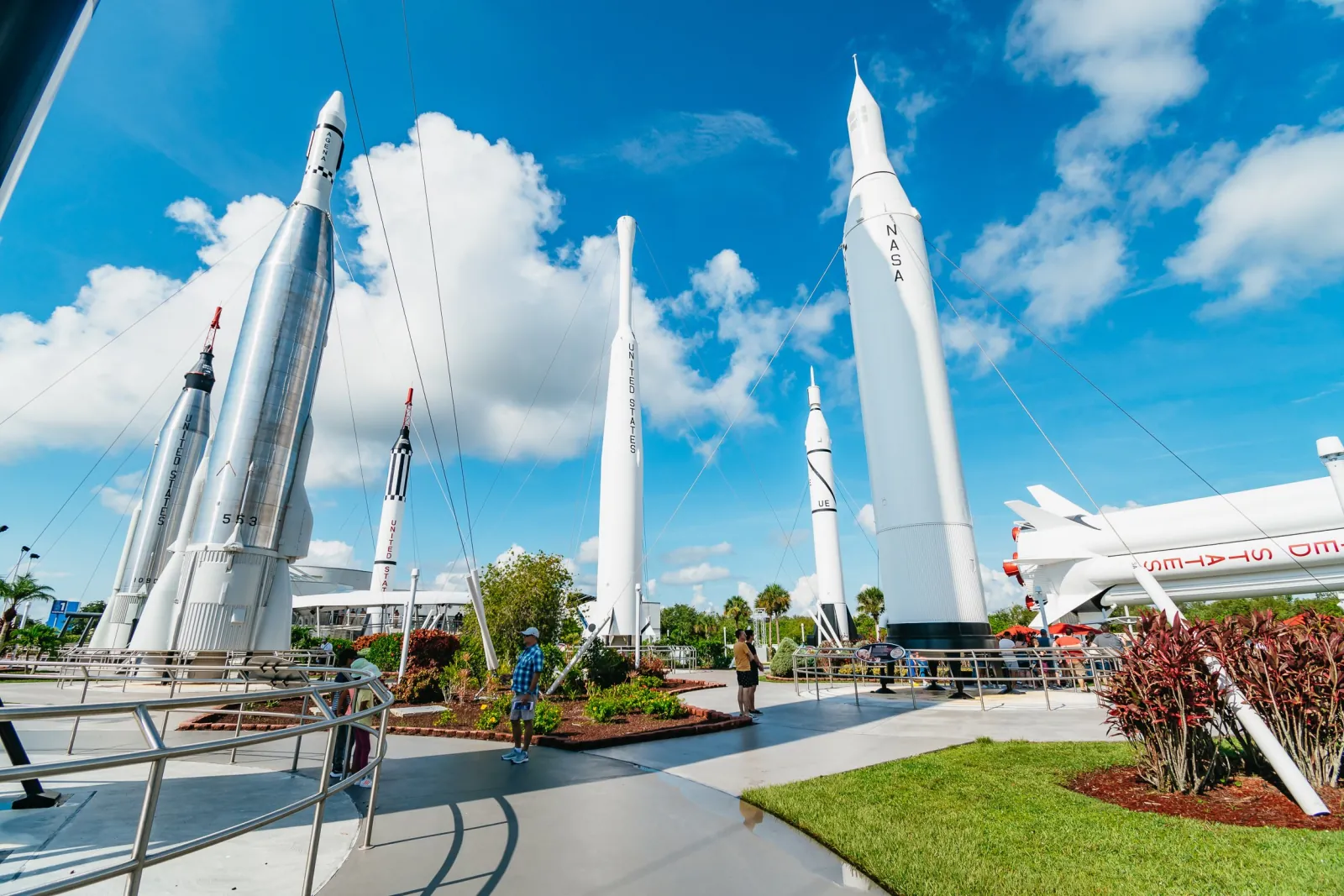 White and silver rockets standing in the outdoor Rocket Garden under a blue sky with visitors on the paths