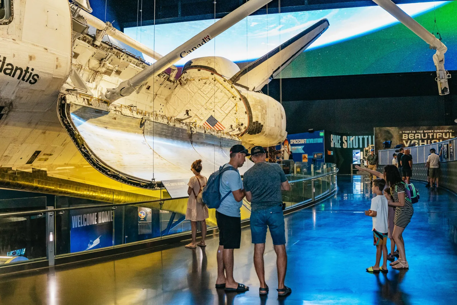 Visitors on a walkway beside Space Shuttle Atlantis, displayed tilted with payload bay doors open and its robotic arm extended