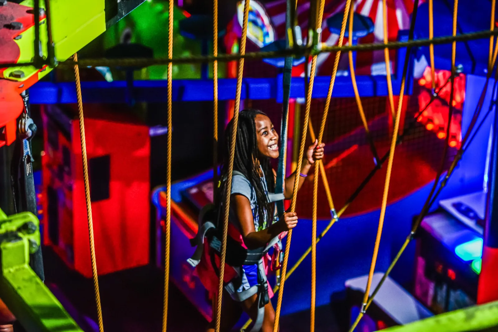 Girl in a harness climbing through the neon-lit glow-in-the-dark ropes course