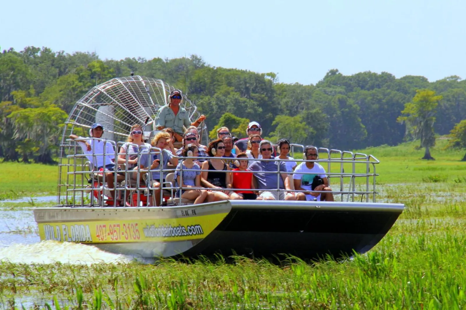 Wild Florida airboat full of passengers wearing ear defenders gliding through marsh grass