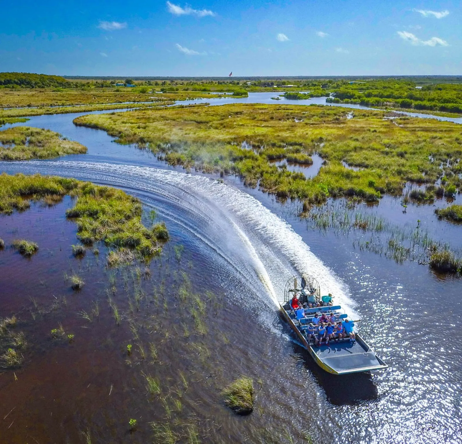 Aerial view of an airboat carving a curved wake through winding marsh channels