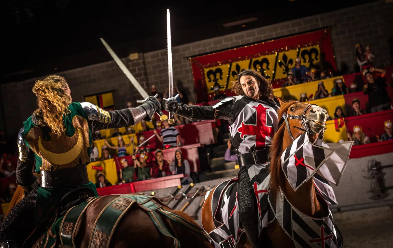 Two mounted knights crossing swords in the Medieval Times arena as the crowd cheers from the stands