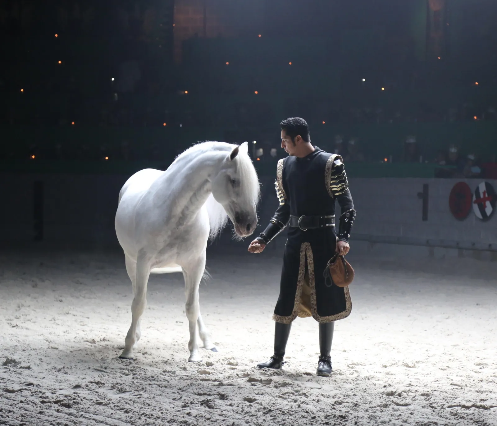 White horse and its trainer in a spotlight during the dressage segment of the show
