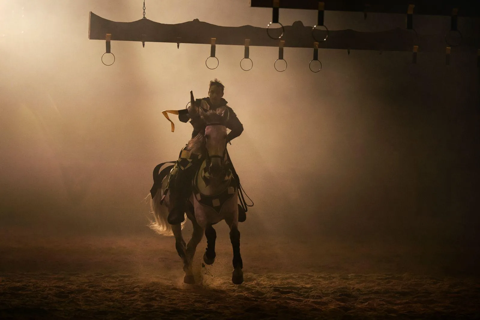Rider galloping through dust toward a row of hanging rings during the ring-spearing game