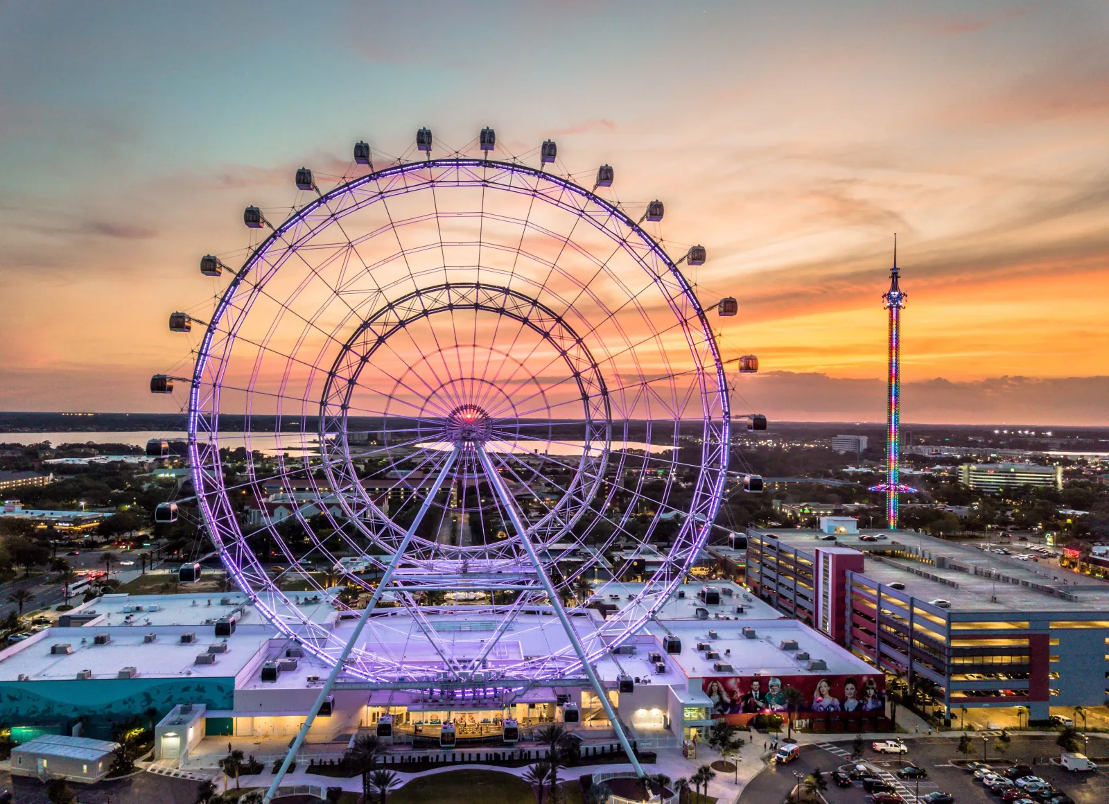 The Orlando Eye lit purple at sunset above ICON Park, with a tall drop tower glowing in the background