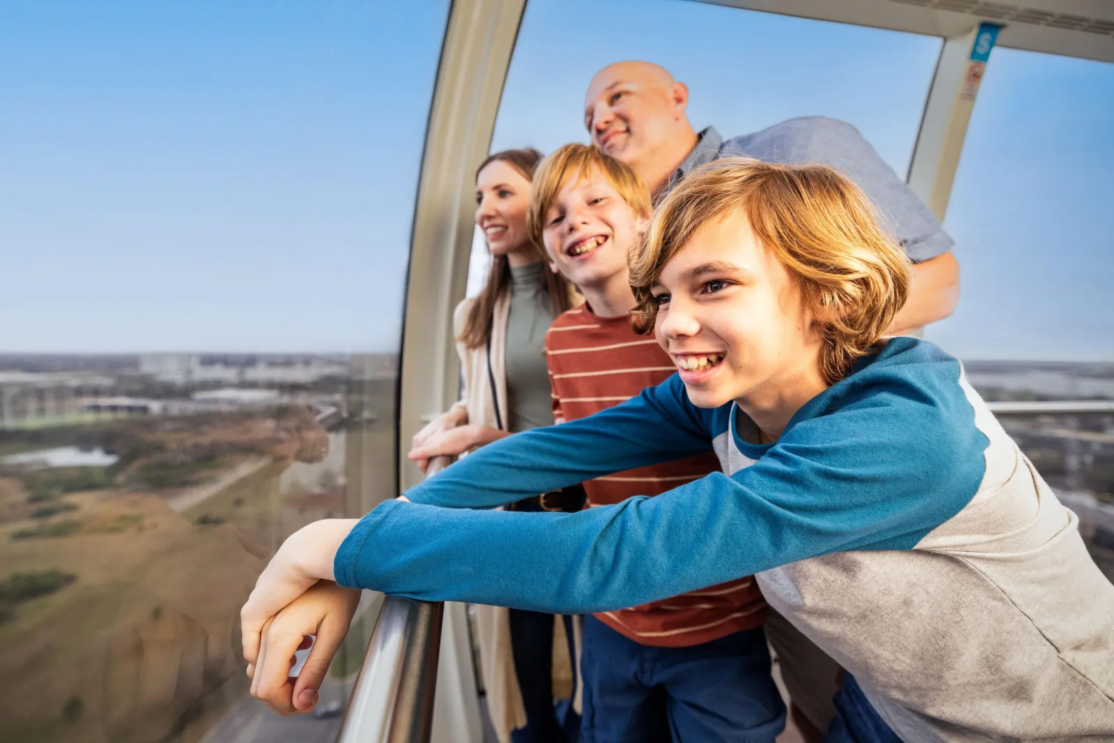 Family leaning on the rail inside an Orlando Eye capsule, looking out over the city