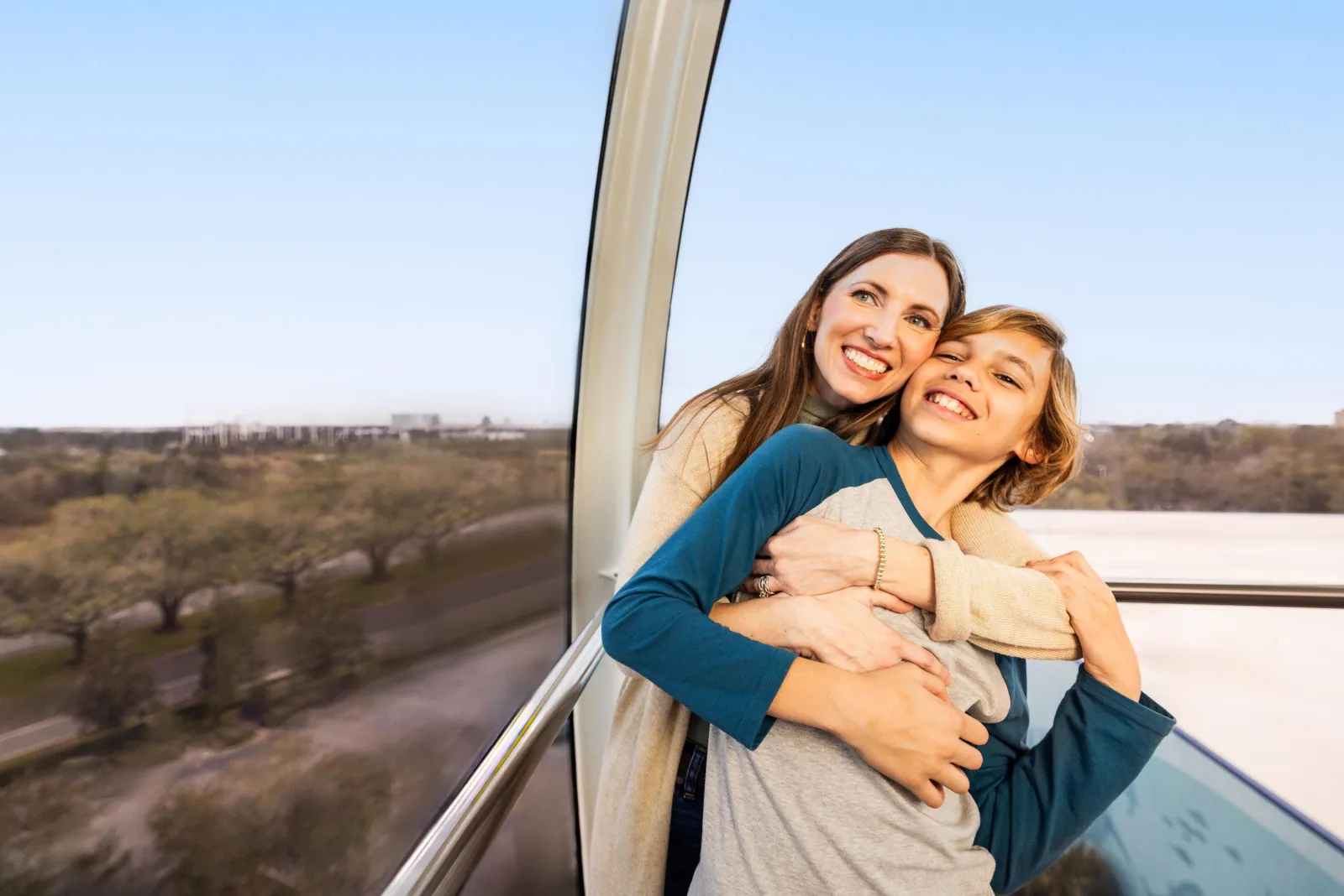 Mother hugging her son beside the curved glass wall of a capsule high above the trees