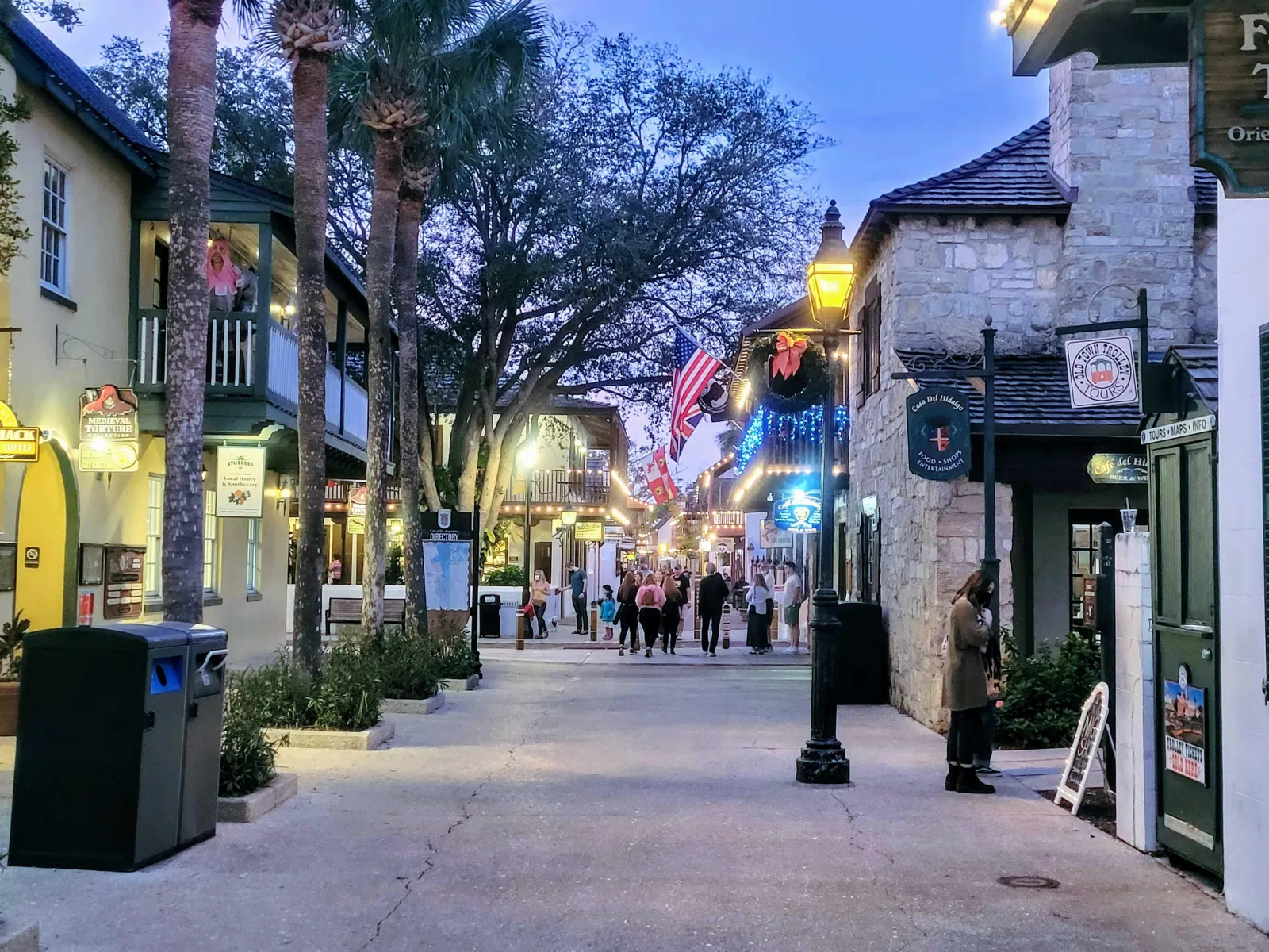 Pedestrian street in St. Augustine's historic district at dusk, with lamps, flags and shop signs