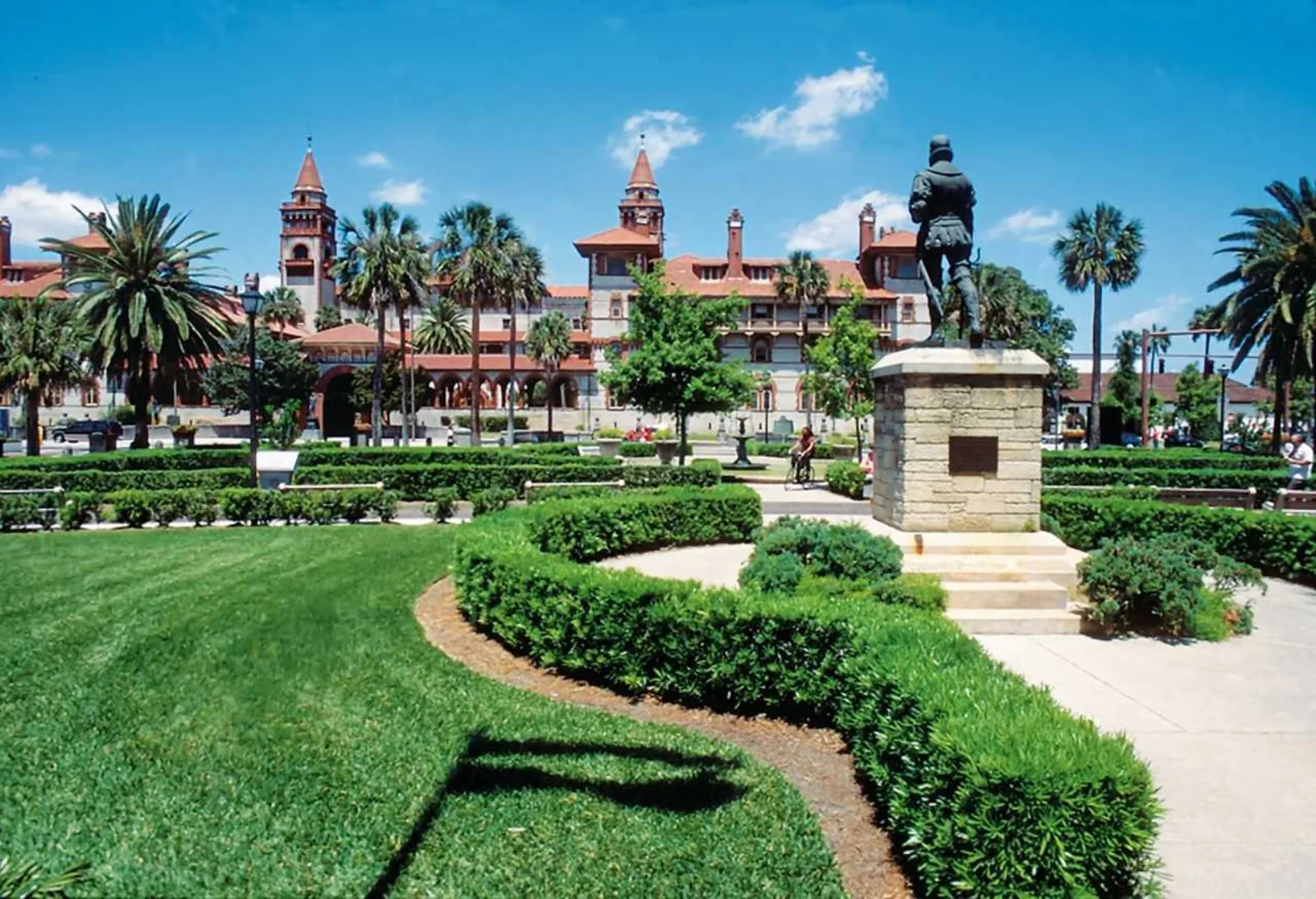 Landscaped plaza with a bronze statue and the towers of Flagler College behind palm trees