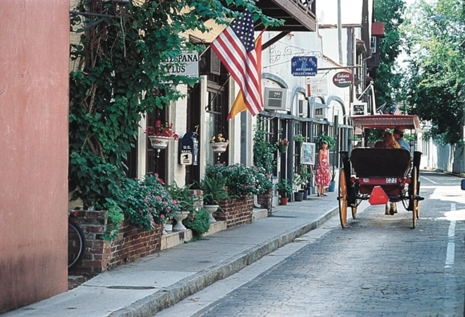 Horse-drawn carriage on a brick street lined with shops, flags and flower boxes