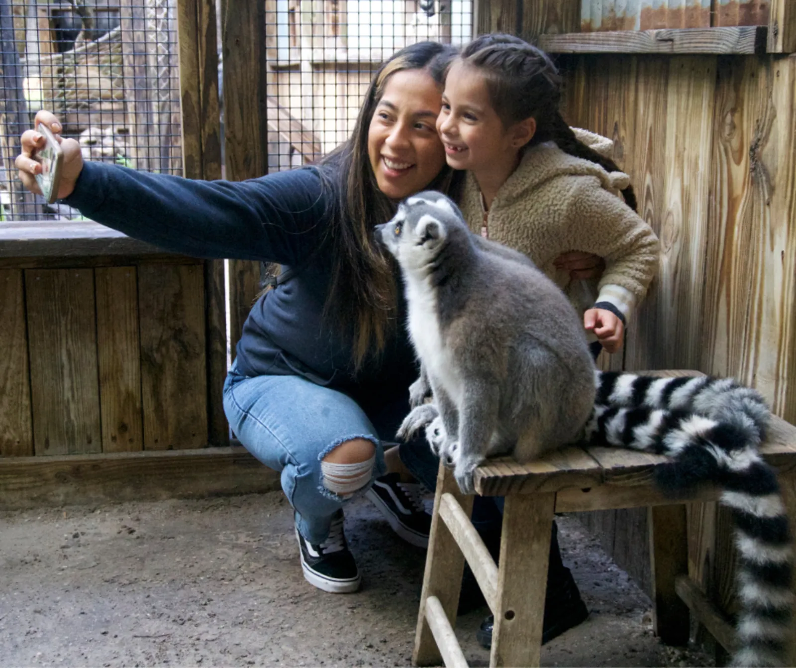 Mother and daughter taking a selfie with a ring-tailed lemur sitting on a bench