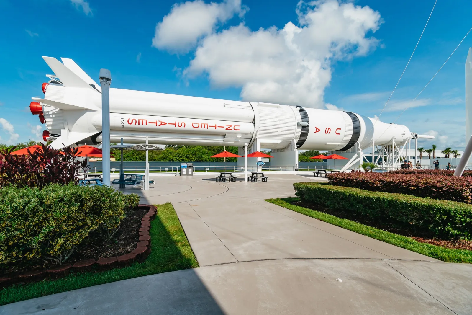 Saturn IB rocket displayed on its side above picnic tables and red umbrellas in the Rocket Garden