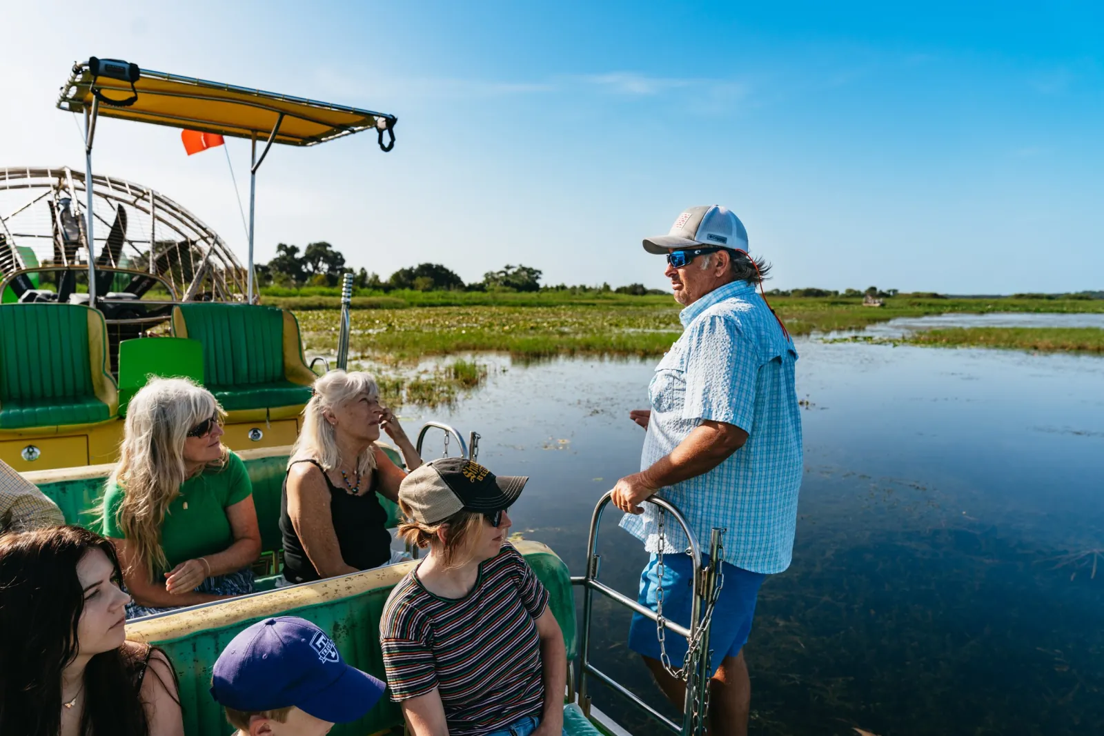 Airboat captain in sunglasses standing at the rail and talking to seated passengers