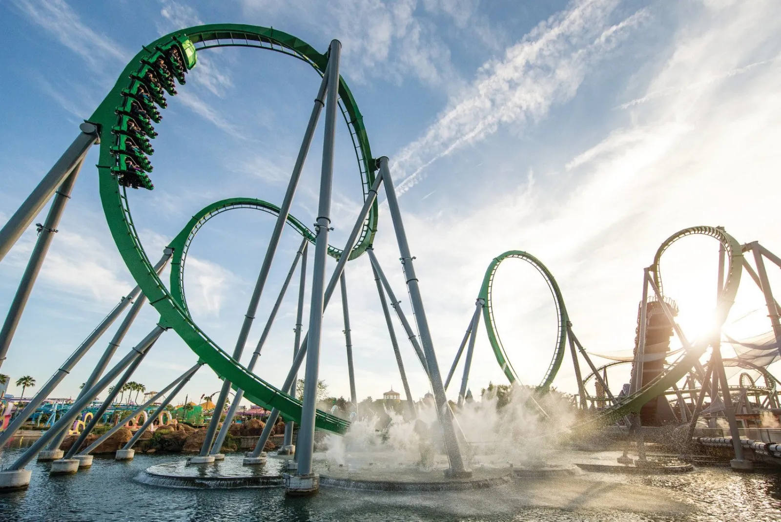 Green loops of The Incredible Hulk Coaster over the lagoon, with a train upside down at the top of a loop