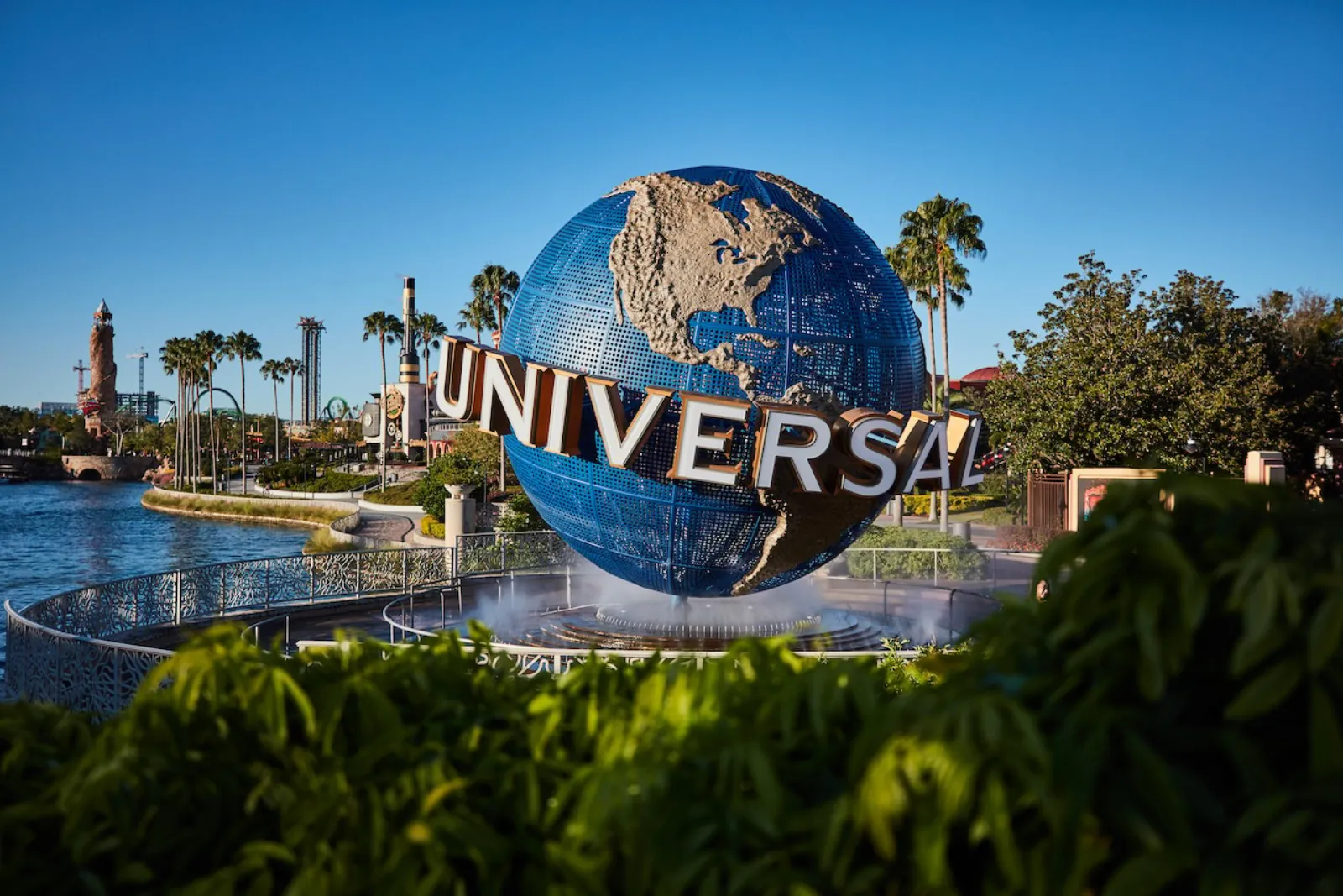 Universal globe on its fountain by the waterway, with palm trees and ride towers in the background