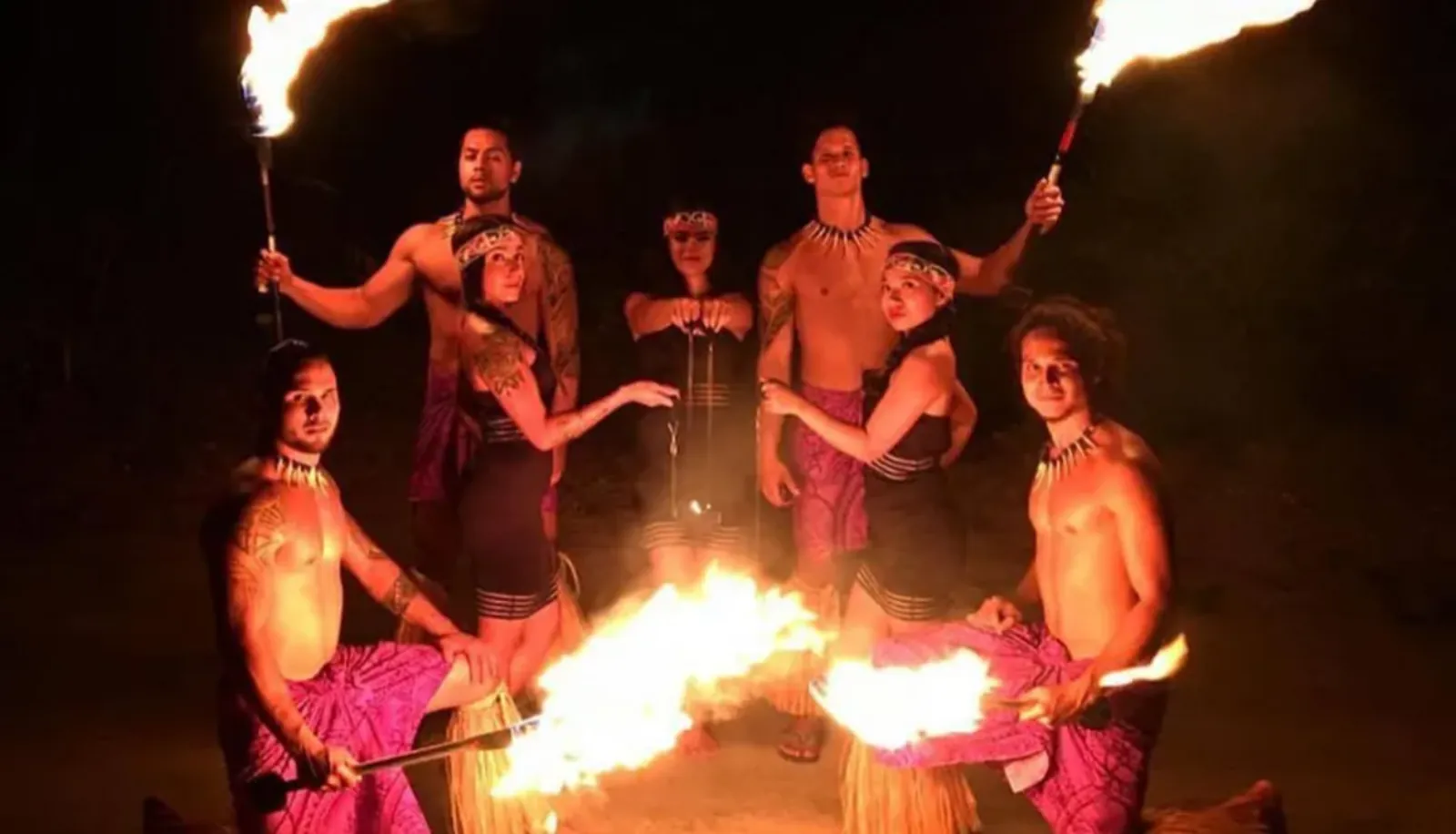 Cast of dancers and fire performers posing at night with flaming torches and fire knives
