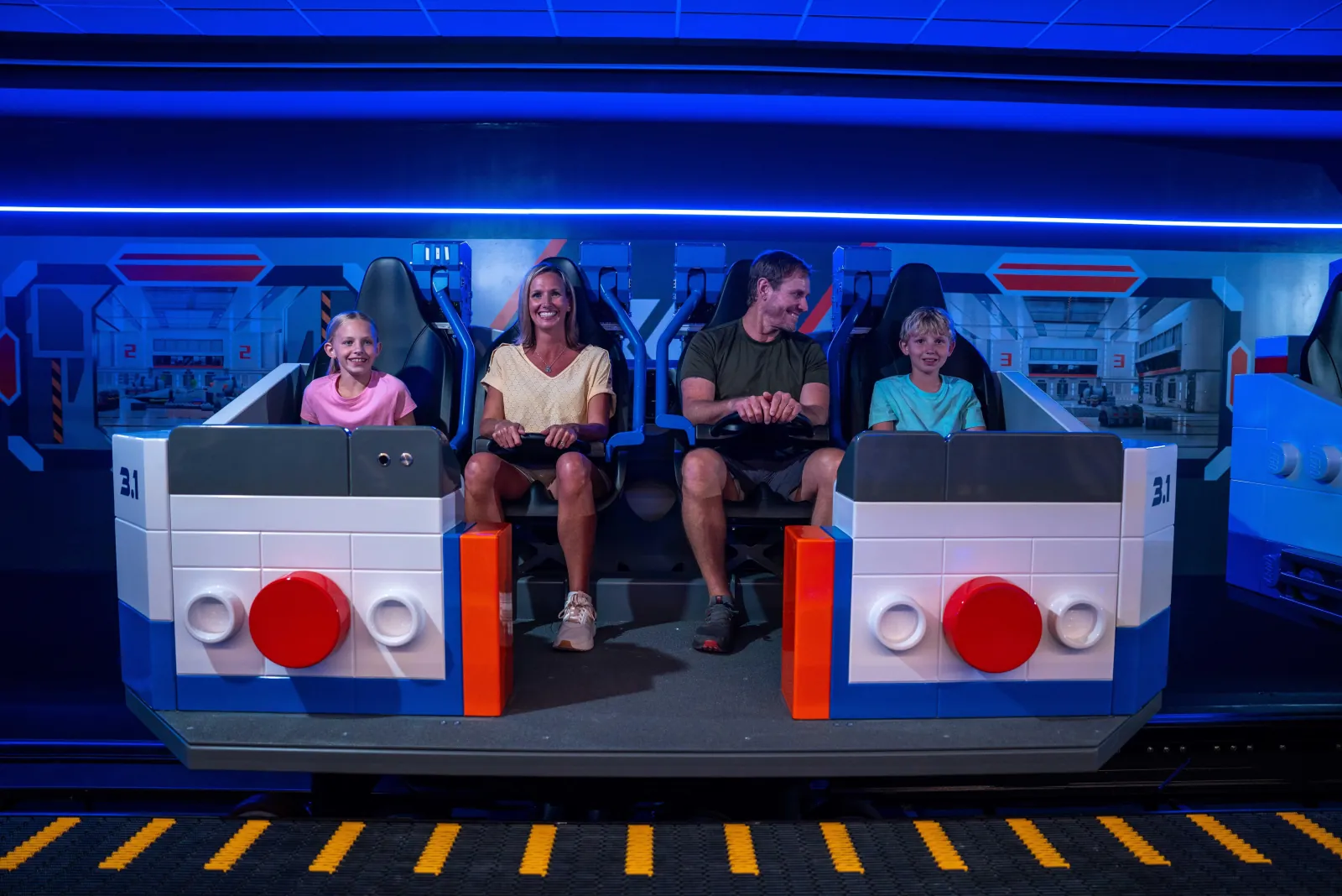 Family of four seated in a white LEGO-style ride vehicle in a blue-lit space-themed station