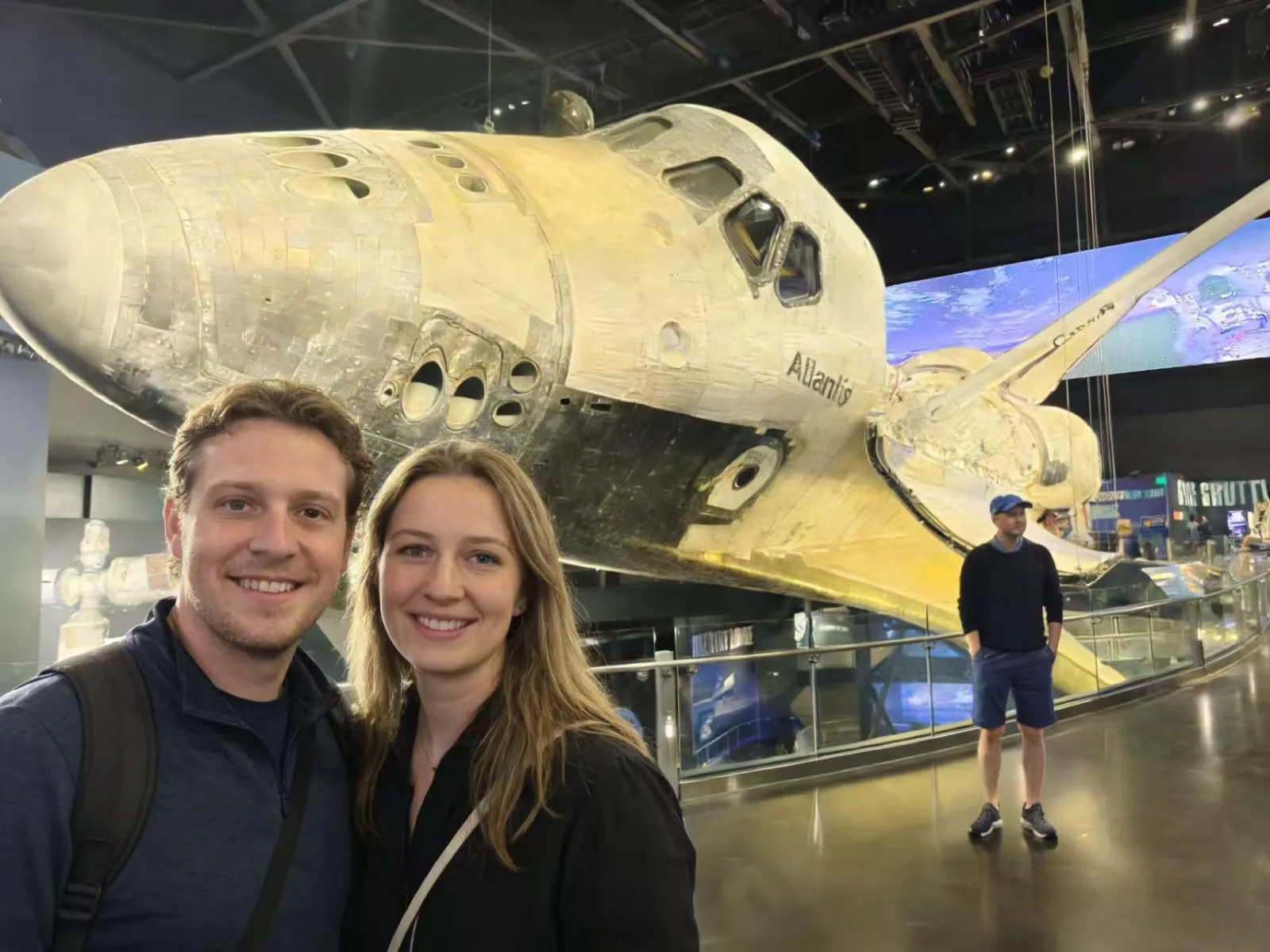 Couple taking a selfie in front of the nose and cockpit of Space Shuttle Atlantis in its exhibit hall