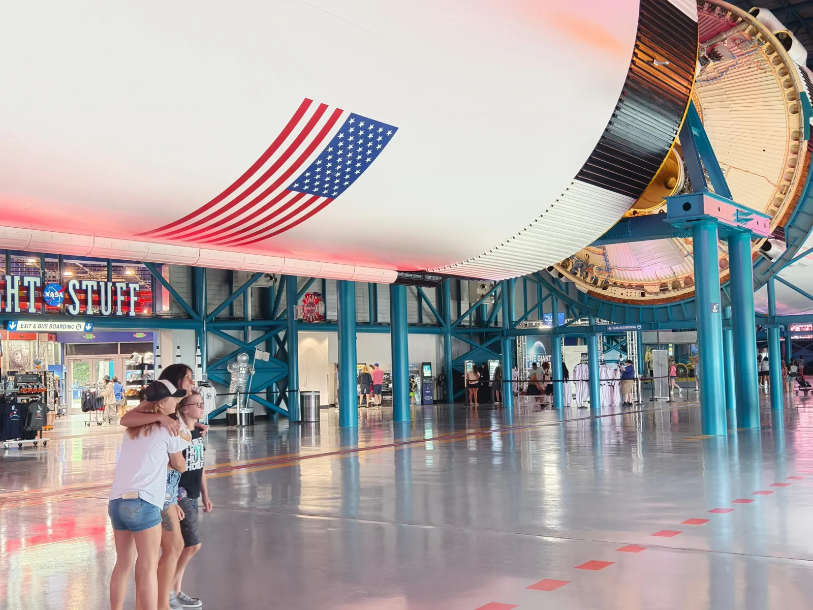 Visitors walking under the underside of the Saturn V inside the Apollo/Saturn V Center, beside the Right Stuff shop