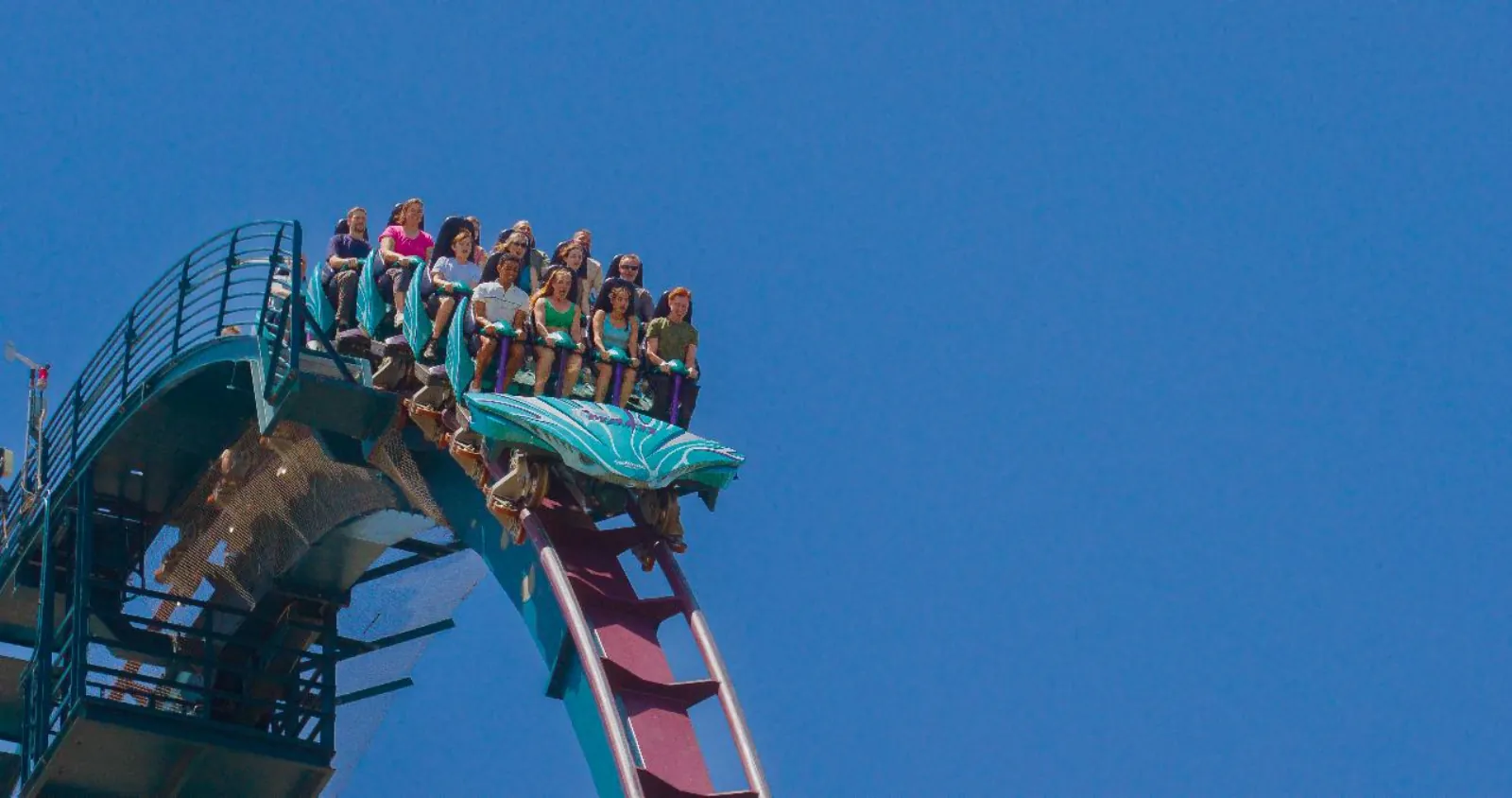 Coaster train cresting the top of a steep drop against a clear blue sky