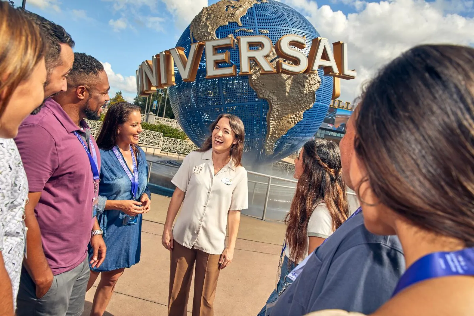 VIP guide in a cream uniform chatting with a lanyard-wearing tour group in front of the Universal globe