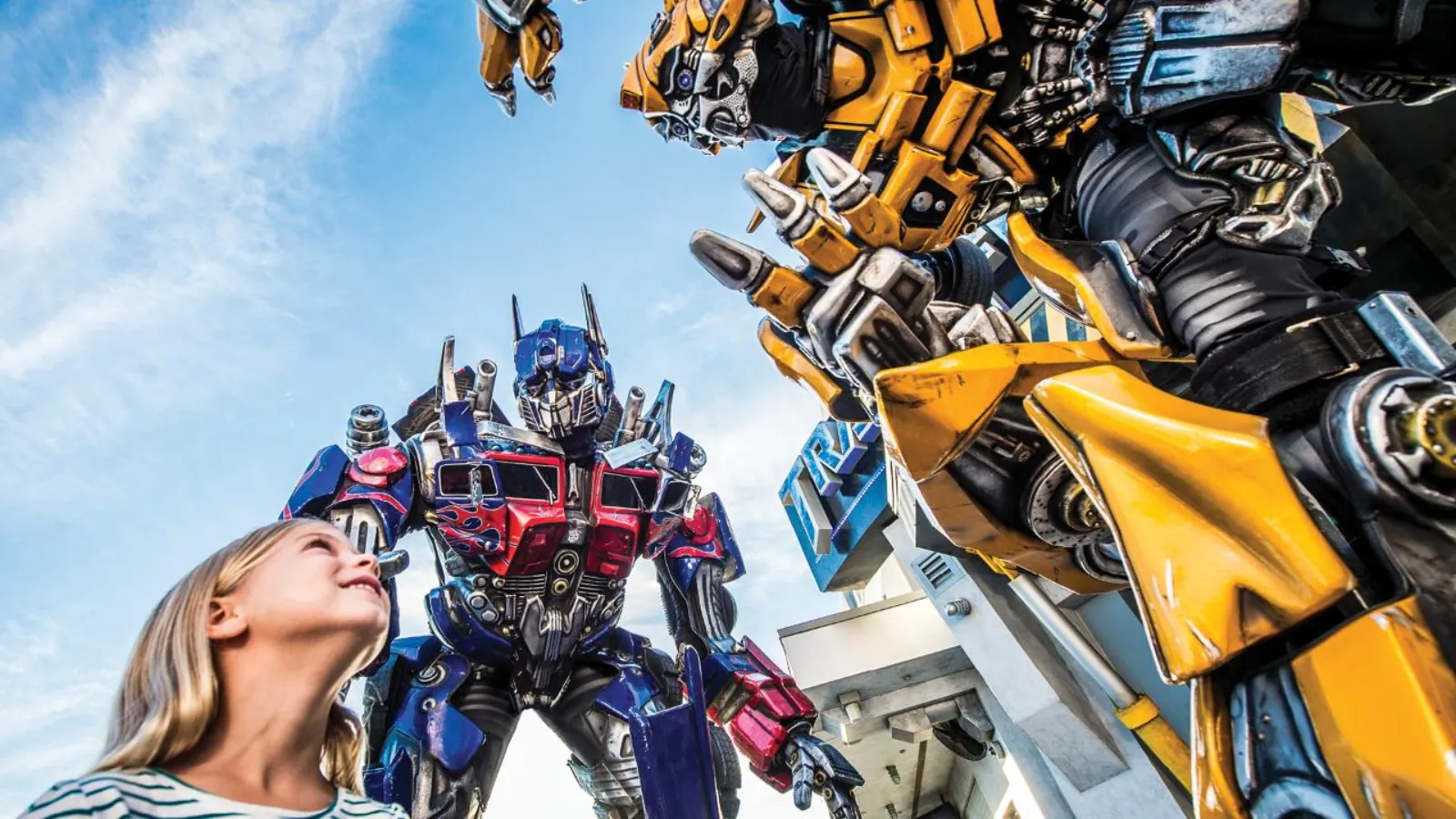 Girl looking up at giant Optimus Prime and Bumblebee figures outside the Transformers ride