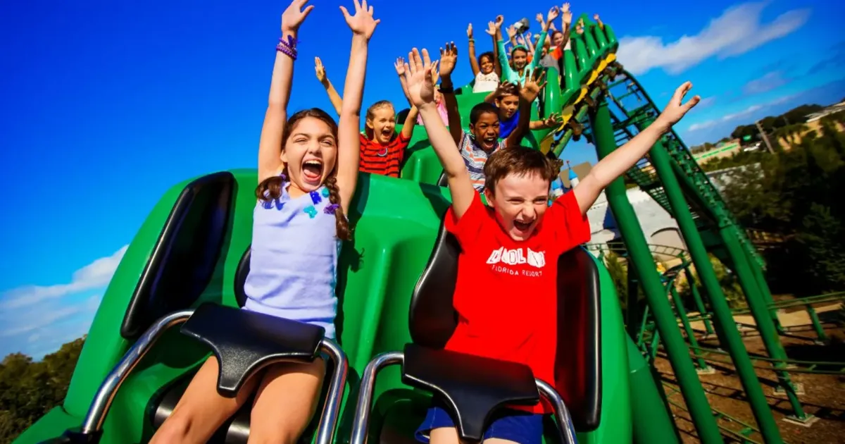 Children with their arms up on a green family roller coaster at LEGOLAND Florida
