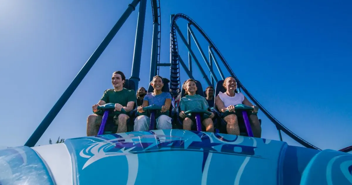 Riders at the top of a blue SeaWorld Orlando roller coaster on a clear day